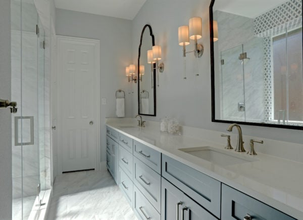 A spacious bathroom featuring a double vanity with light gray cabinets, marble countertops, and elegant black-framed mirrors flanked by wall sconces.