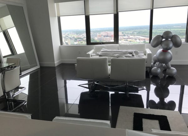 A high-rise apartment living area with polished black floors, large windows, minimalist white furniture, and a metallic sculpture.