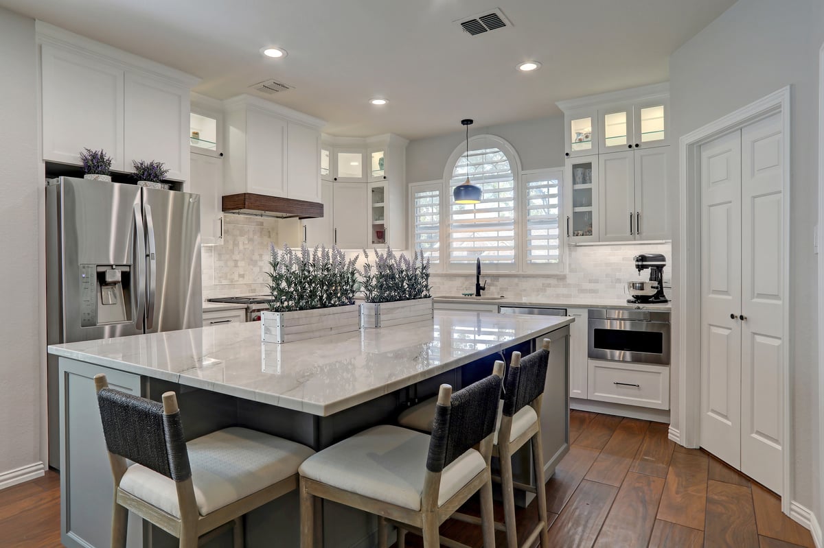 A contemporary kitchen featuring an expansive central island, stylish cabinetry, and stainless steel appliances, —all adorned in a sleek white finish for a modern and sophisticated look.