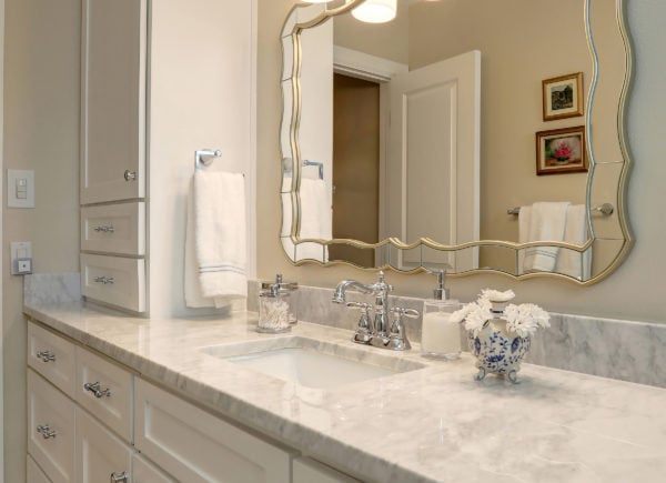 A bathroom with a large vanity, cream-colored cabinets, marble countertop, and a unique wavy-edged mirror above the sink.