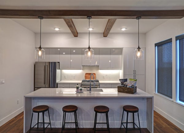 A contemporary kitchen with white cabinets, a large island with bar stools, and exposed wooden beams, complemented by pendant lighting.