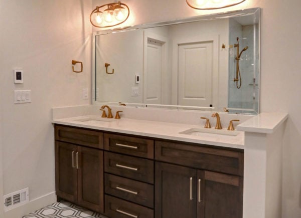 A neatly presented bathroom with a wide mirror, dark wooden vanity with double sinks, and golden fixtures.