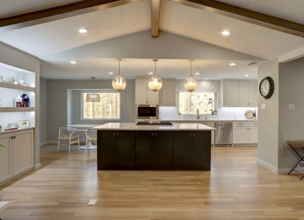An open-plan kitchen and dining area with a black island, white cabinetry, wooden flooring, and globe pendant lights hanging from a vaulted ceiling.