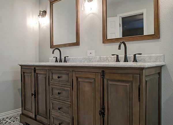 An elegant bathroom with a large, ornate mirror over a vintage-style vanity with a marble top and dark faucets.