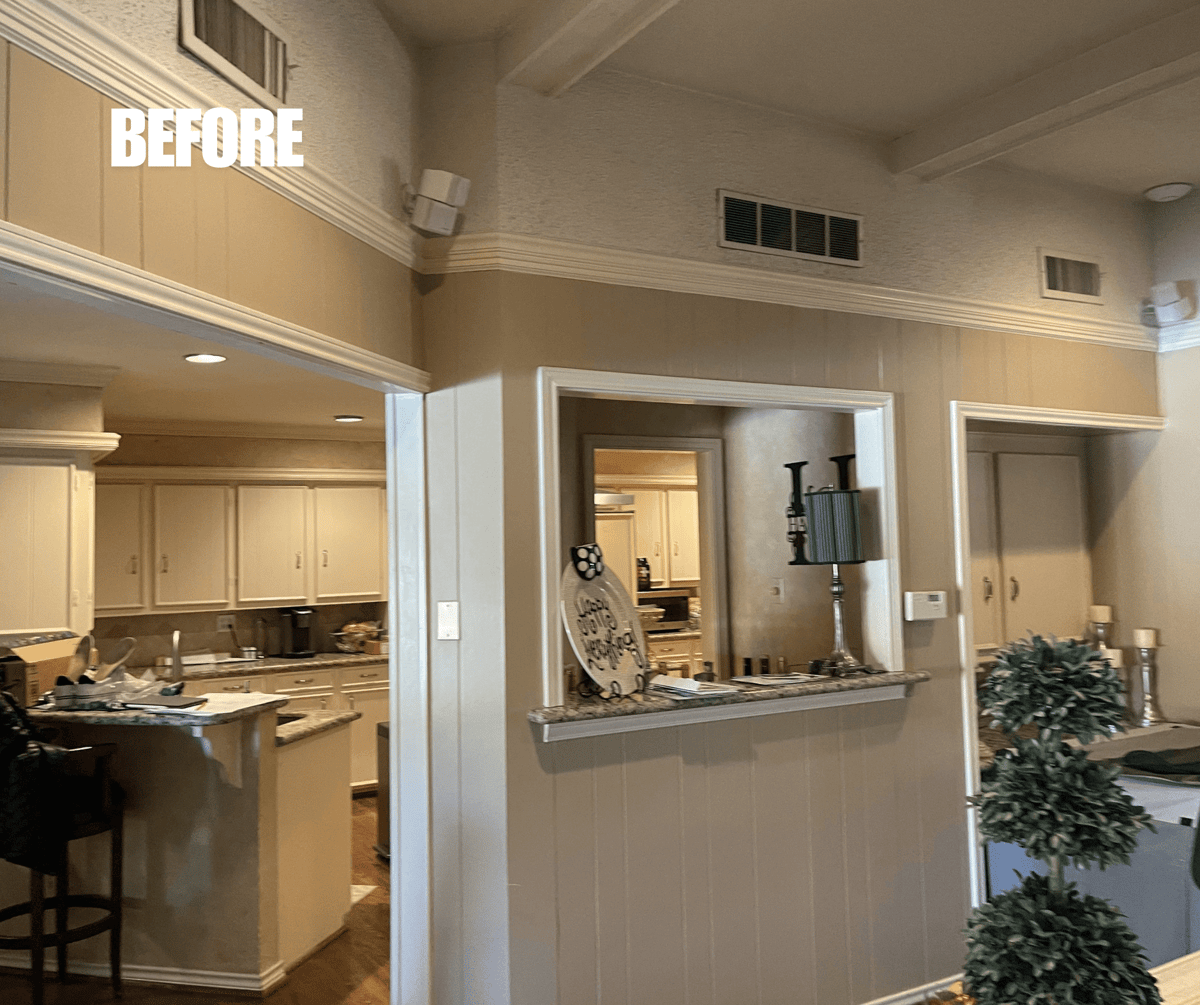 BEFORE: Interior view of a house showing a kitchen and hallway, featuring wood paneling and ceiling beams.