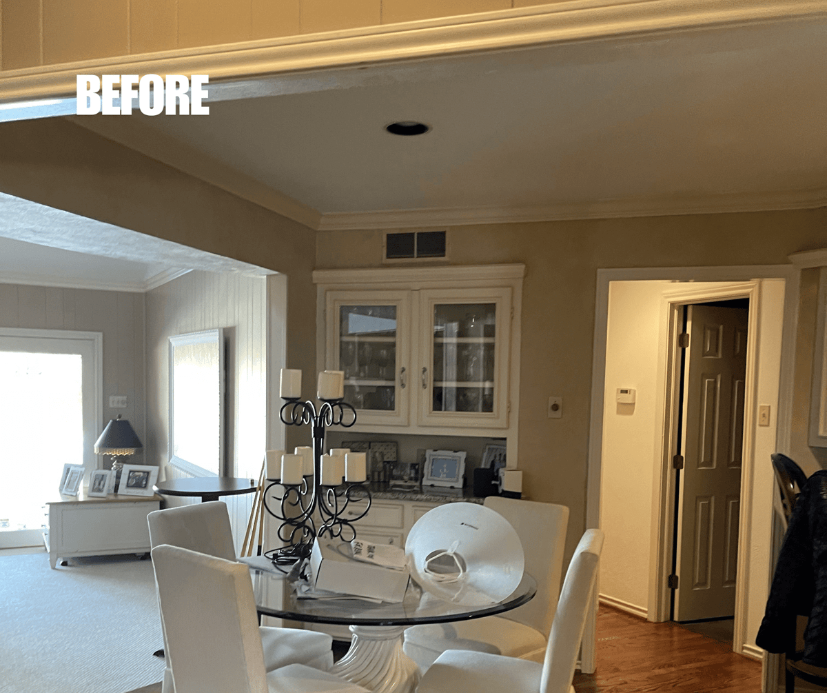 BEFORE: Dining area with white furniture, decorative candle holder on a glass table, and built-in cabinets. An open door and a hallway are visible.