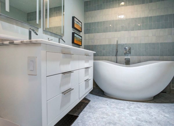 A contemporary bathroom with a floating white vanity, unique freestanding bathtub, and grey square-tiled walls.