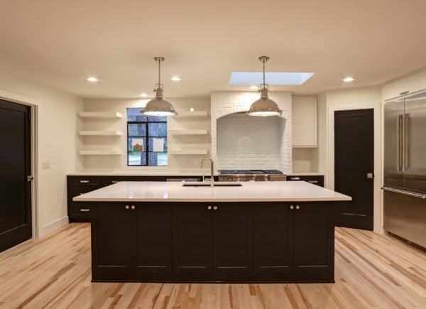 A modern kitchen with a large central island, sleek dark cabinets, stainless steel appliances, and two industrial-style pendant lights.