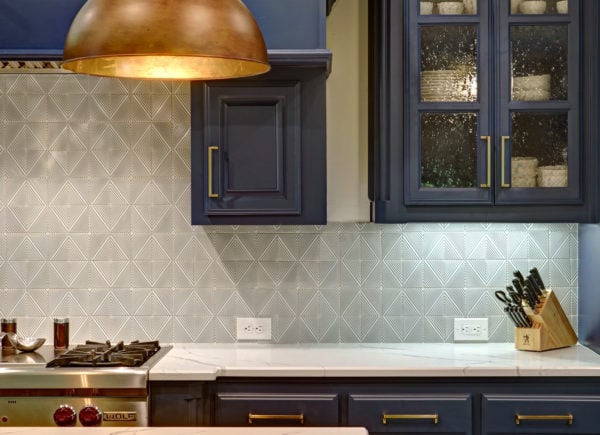 A stylish kitchen corner with navy blue cabinets, a brass dome pendant light, and a geometric patterned backsplash.