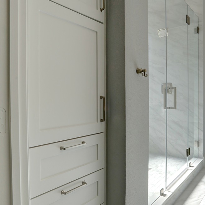 A partial view of a white bathroom cabinet, showcasing the cabinet's design and hardware.