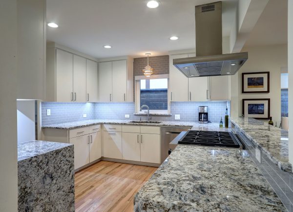 A modern kitchen with white cabinetry, granite countertops, a central island, and stainless steel appliances.