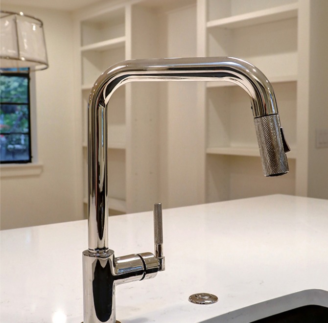 A modern kitchen faucet with a chrome finish, featuring a high arc and a pull-down spray head, set against a white countertop.