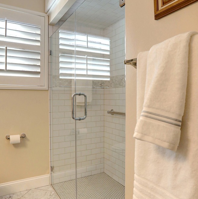 A bathroom shower area with subway tiles and a built-in niche for toiletries. A towel hangs on a rack outside the glass shower door.