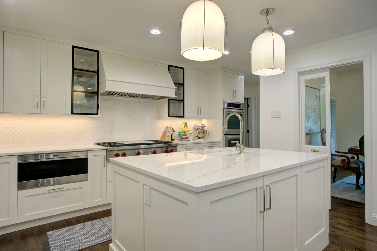 A modern kitchen with white cabinets, a quartz island, stainless steel appliances, and two pendant lights. Located in North Dallas, Texas.