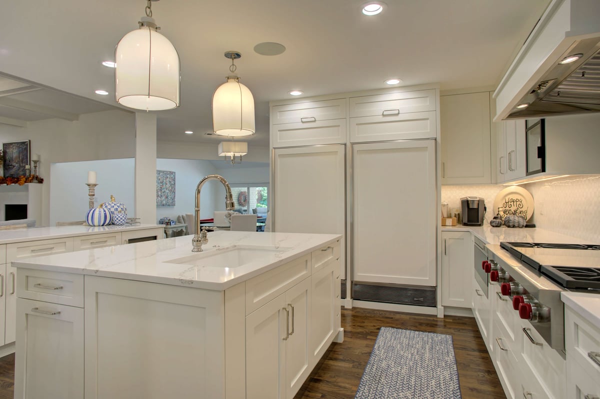 A modern kitchen features white cabinetry, a large island with pendant lights, and stainless steel appliances, including a six-burner stove and double door refrigerator.