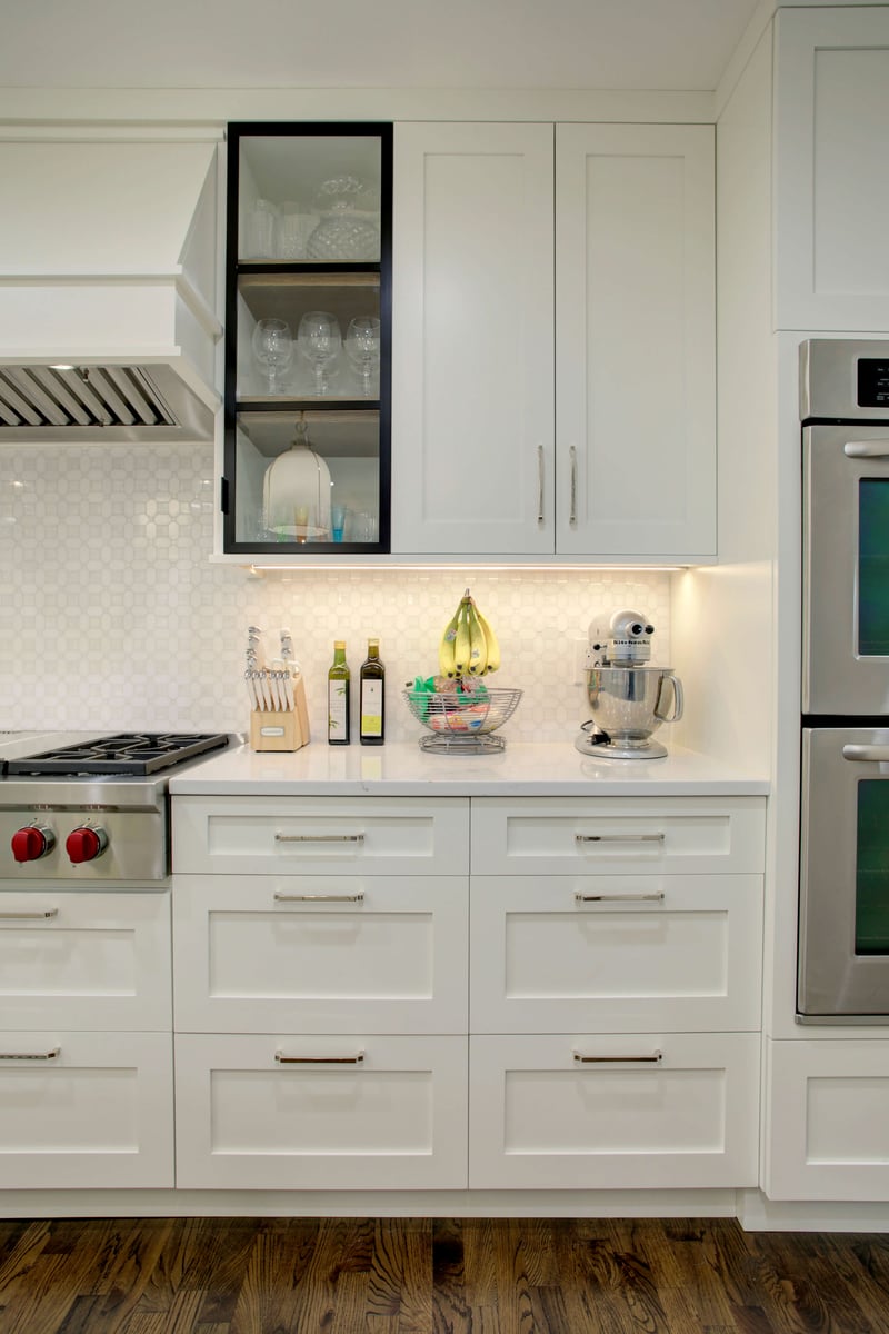 Modern kitchen with white cabinets, stainless steel oven, stovetop, and a mixer on the counter. The backsplash features a hexagonal tile pattern, and kitchen utensils are neatly arranged.