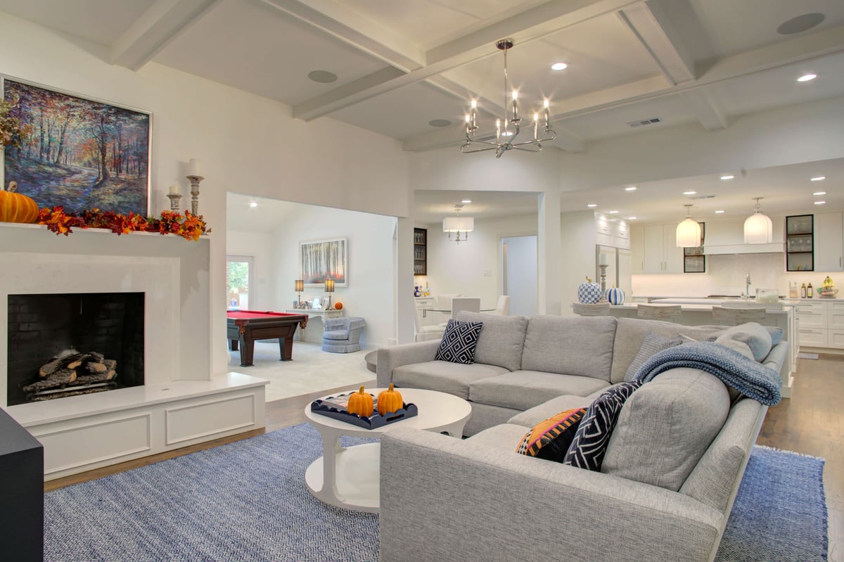 Spacious living room with a gray sectional sofa, round table with pumpkins, and a fireplace. Open floor plan extends to the kitchen, dining area, and game room with a billiard table.