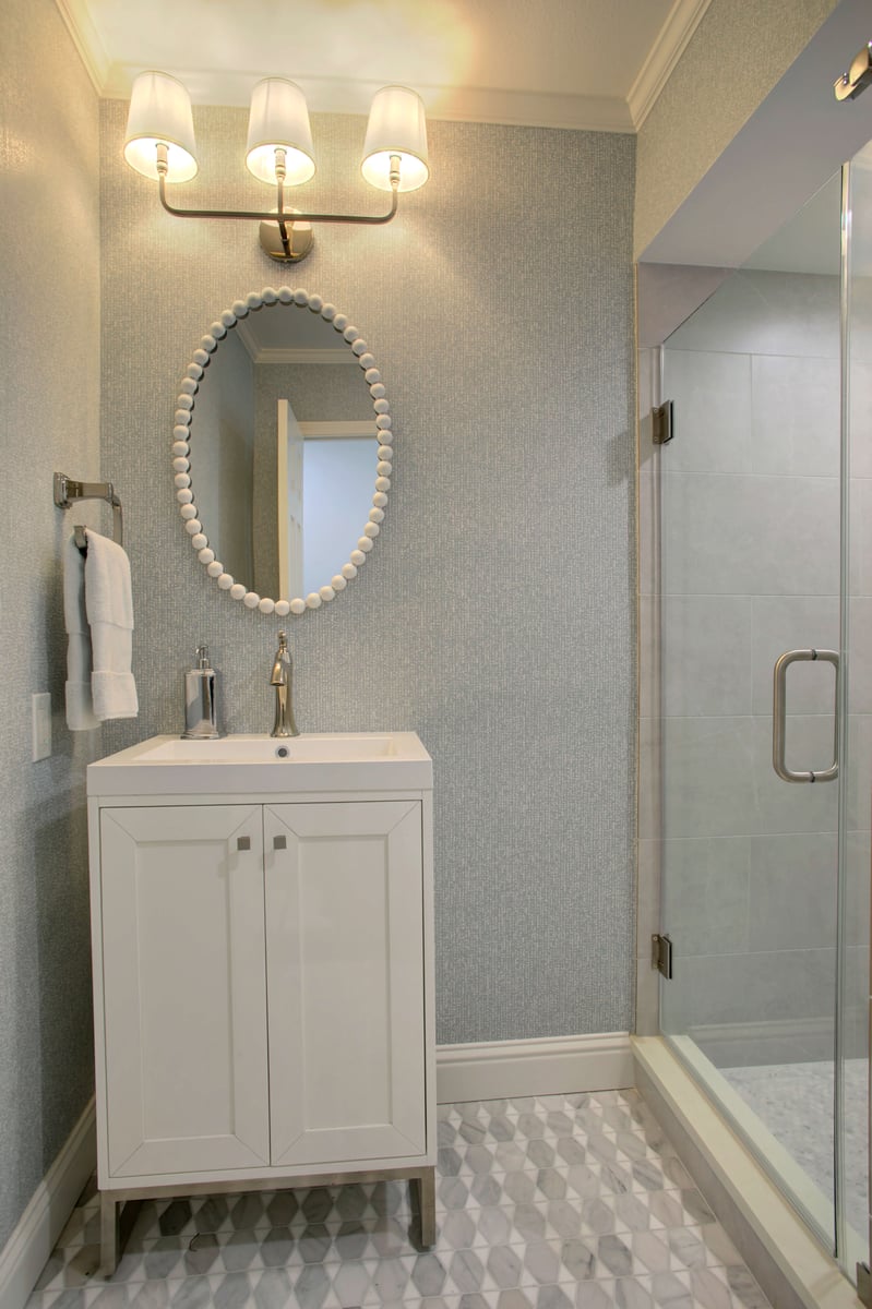 A modern shower in North Dallas with light gray large profile tile walls, a metallic showerhead, and a built-in shower cubby to hold toiletries.