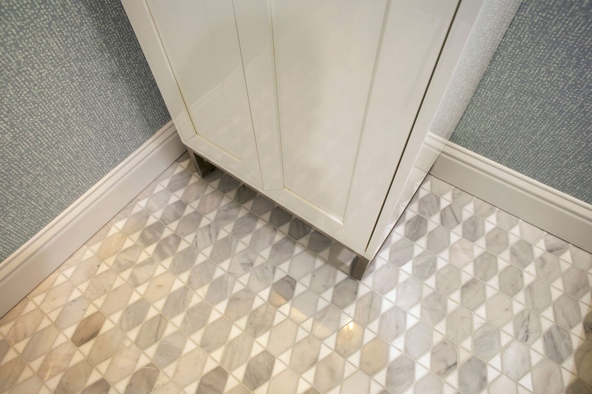 A white cabinet sink stands in a corner on a geometric-patterned tile floor with textured wallpaper walls. Located in North Dallas, TX