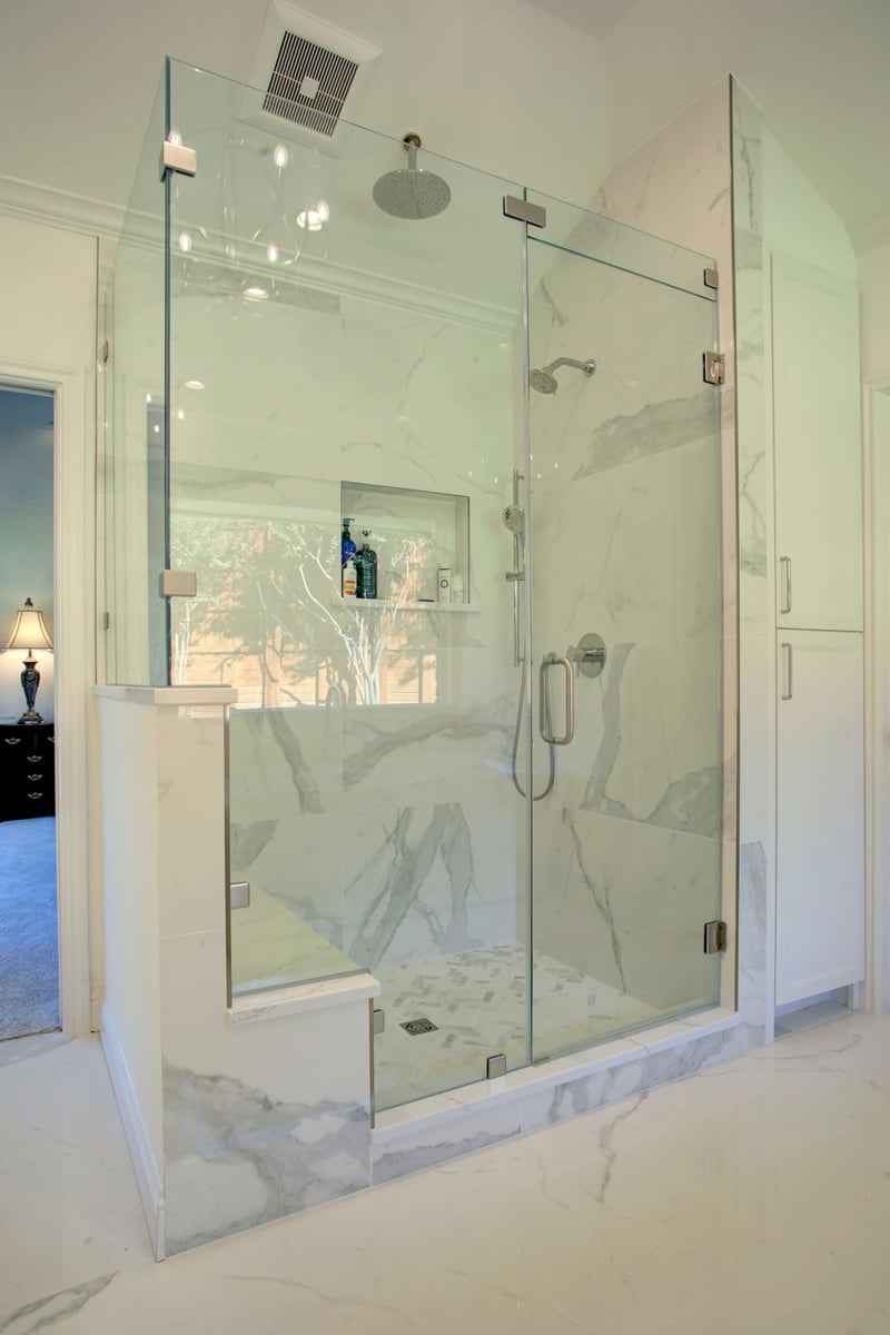 Modern glass shower with a built-in bench, marble-pattern walls, and a rainfall showerhead.