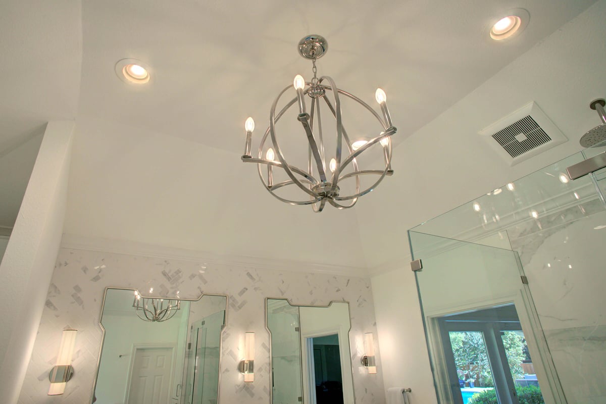 Modern bathroom with a metallic chandelier, two rectangular mirrors, wall sconces, and a glass shower.