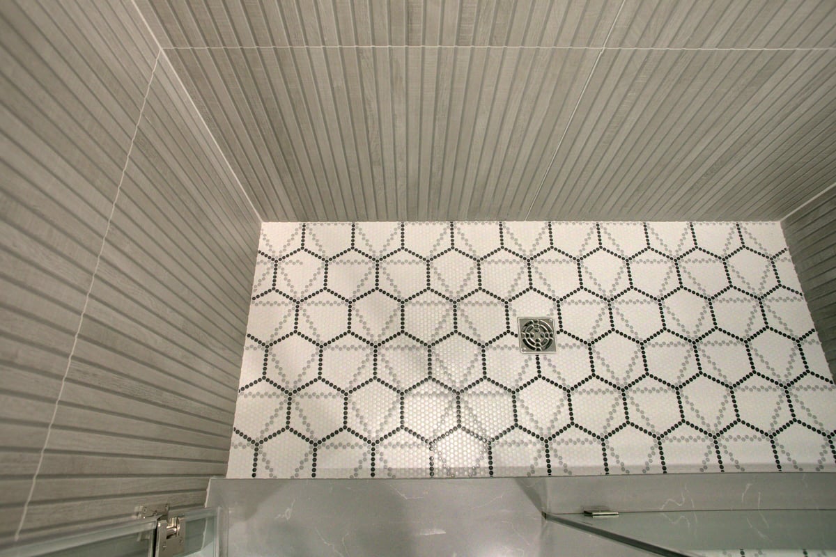 Shower with hexagonal tile floor and gray striped wall tiles, visible drain in the center.