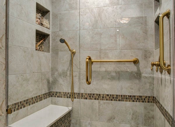 A modern shower with marble tiles, built-in shelves, and gold-colored fixtures, including a handheld shower head.
