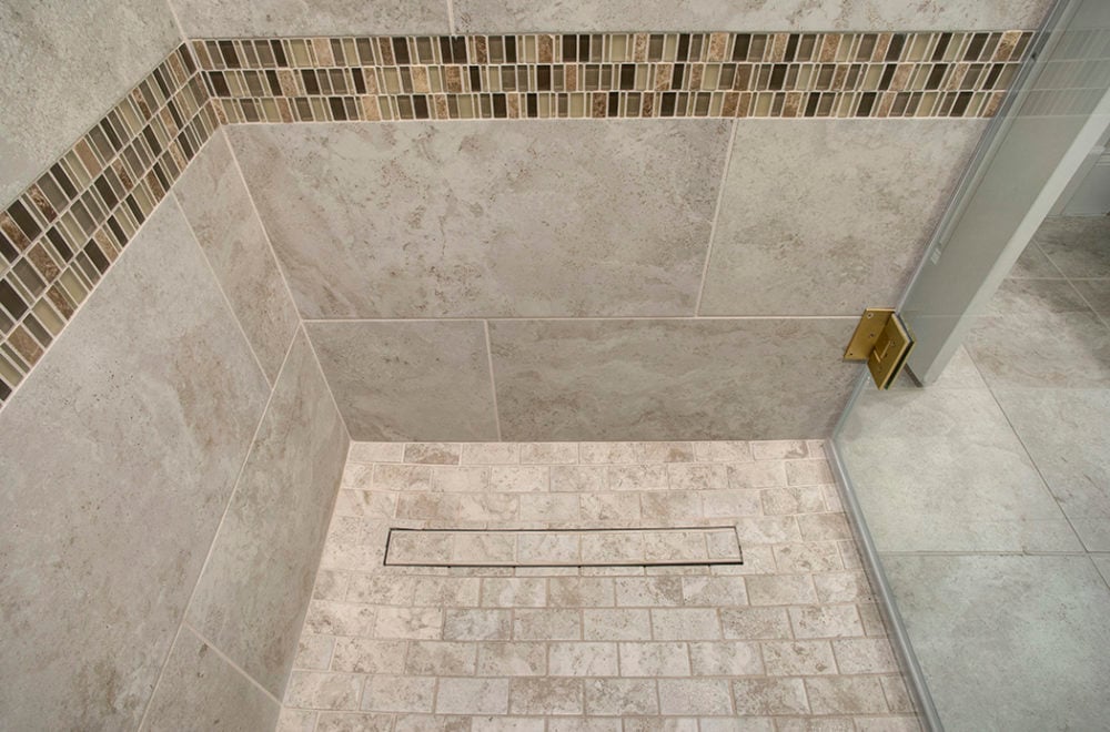 An overhead view of a walk-in shower with marble tiles. The shower floor has a herringbone pattern, and there is a built-in corner bench.