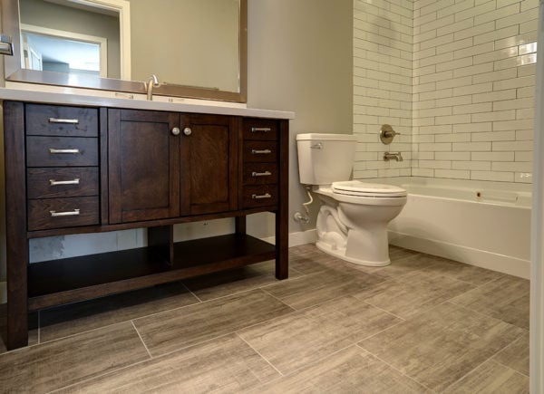 A classic bathroom featuring a dark wood vanity with a stone countertop, white subway tiled wall, and a built-in bathtub.