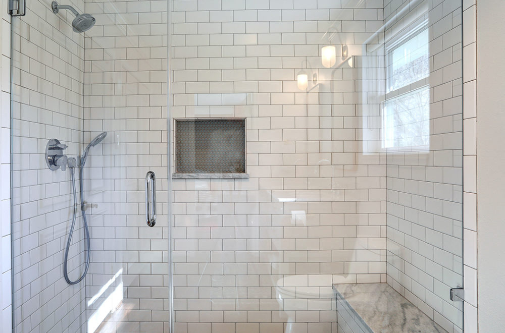 A shower space with white subway tiles, featuring a built-in niche with penny tiles and modern shower fixtures.