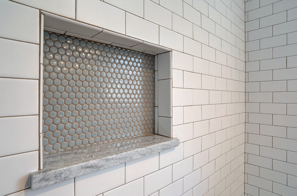 Detail of a shower niche with circular penny tiles in shades of gray and a marble shelf.