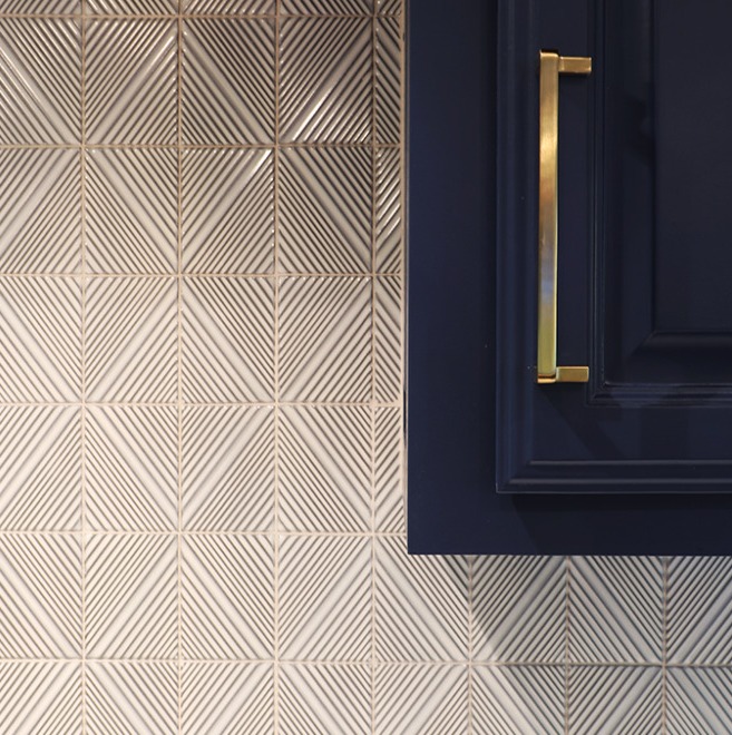 A close-up of a kitchen wall featuring a detailed, white geometric tile backsplash that creates a herringbone pattern.